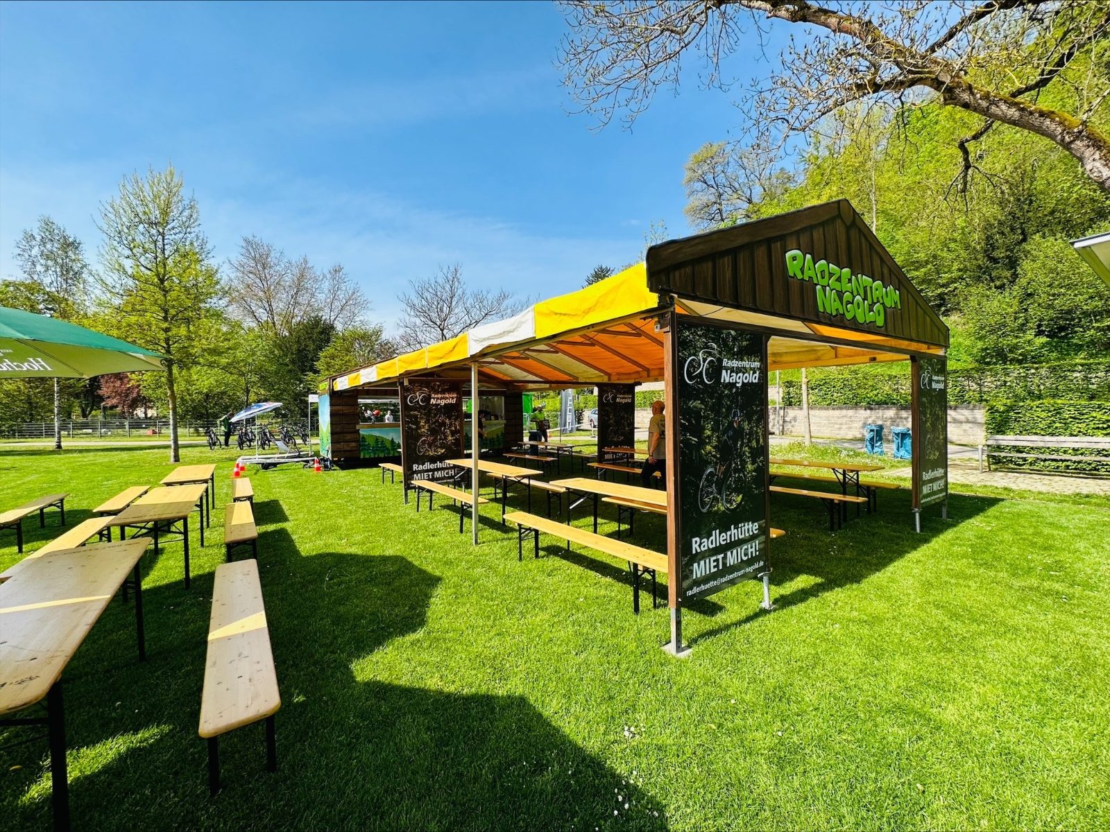 Radlerhütte mit Zelt und Bierbänken auf der Wiese